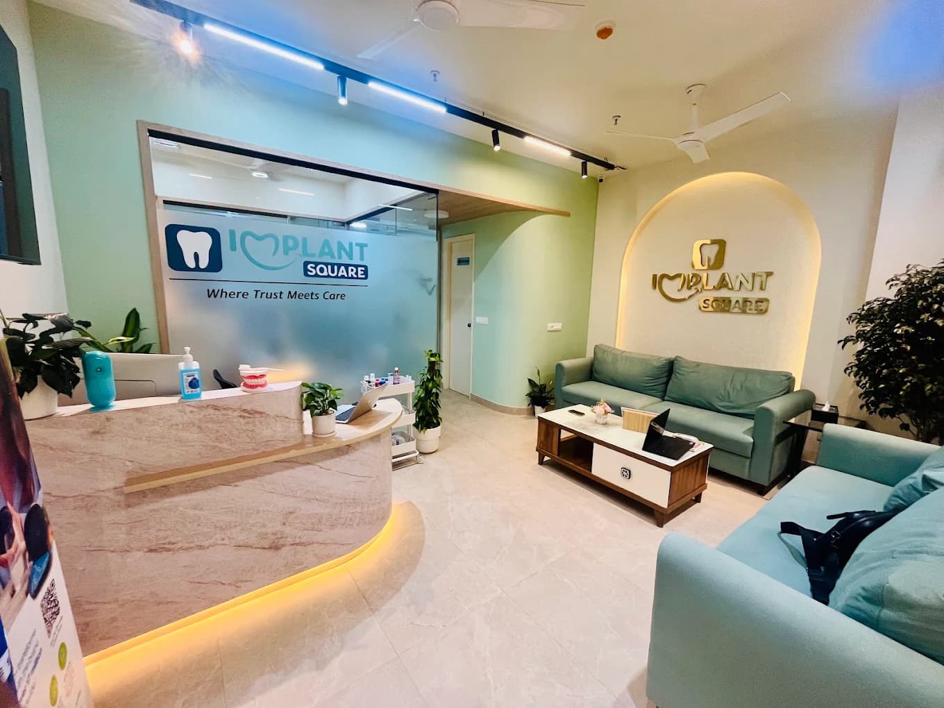 Implant Square Dental reception and waiting area with curved marble desk, teal sofas, plants, and frosted glass showing the clinic logo and tagline Where Trust Meets Care.