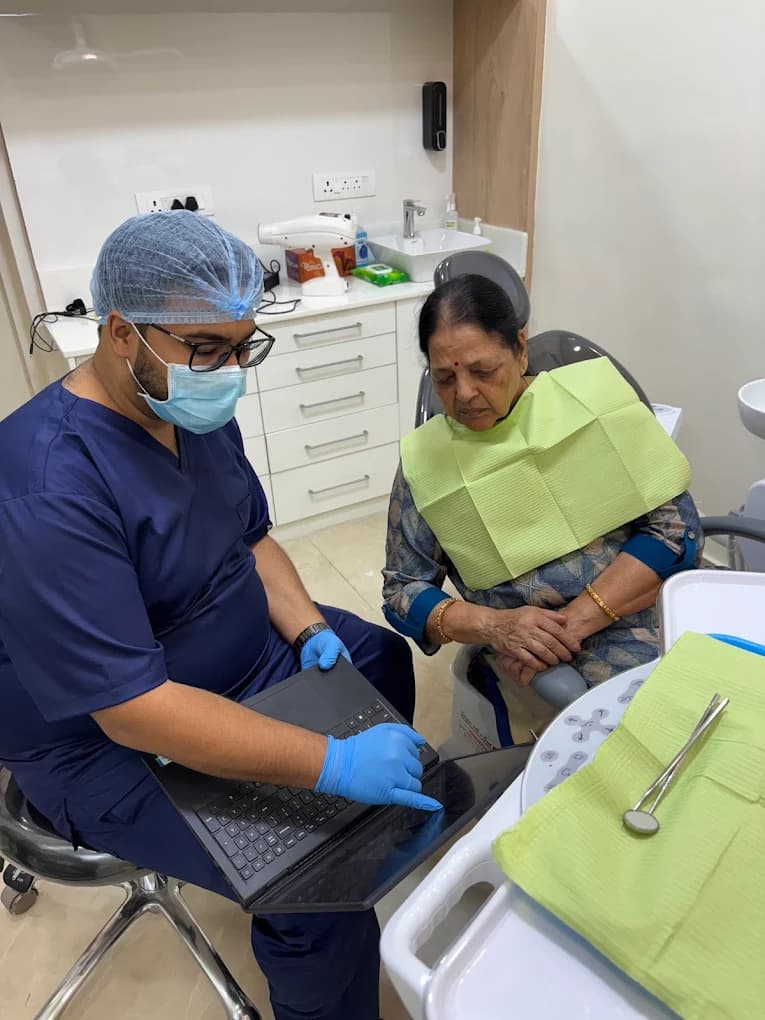 Dentist in protective gear showing a laptop screen to a seated patient in the dental chair during a consultation at Implant Square Dental.